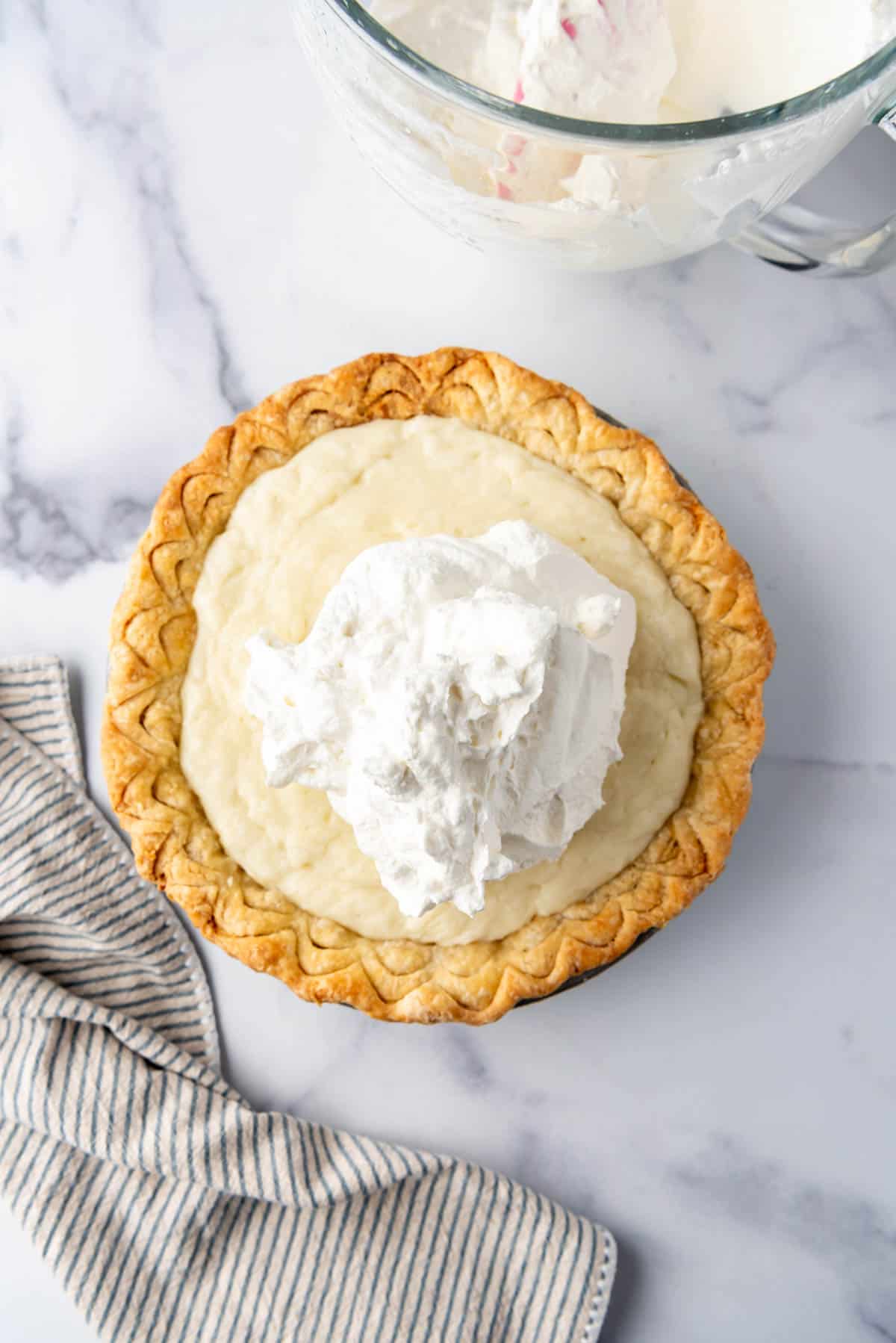 Adding whipped cream to the top of a coconut cream pie.