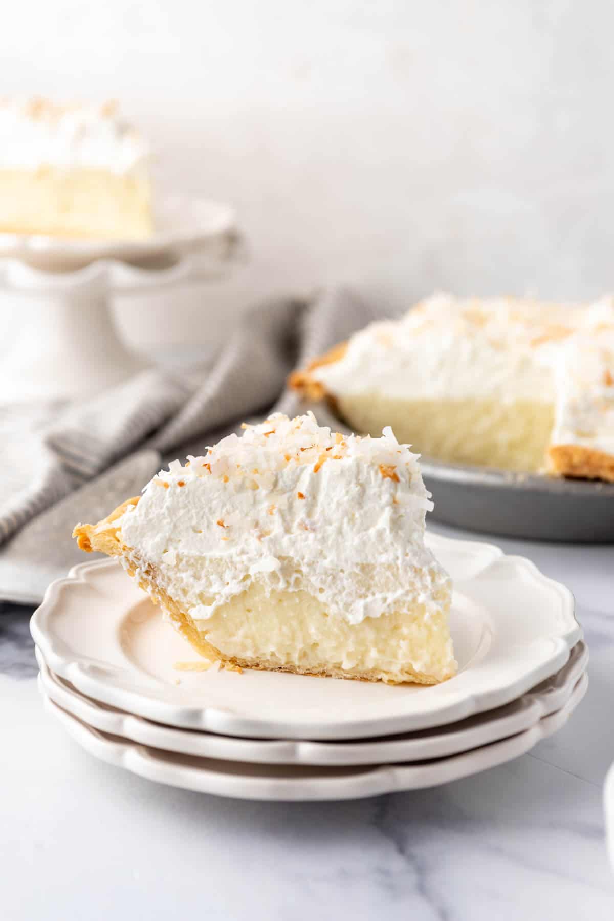 A slice of coconut cream pie on stacked plates.