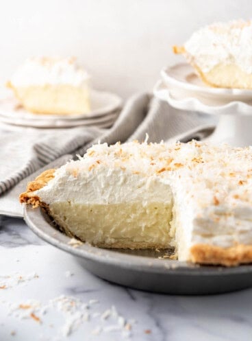 A coconut cream pie with slices removed and placed on plates to the side.