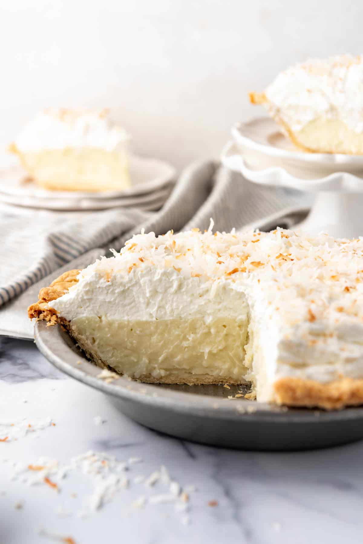 A coconut cream pie with slices removed and placed on plates to the side.