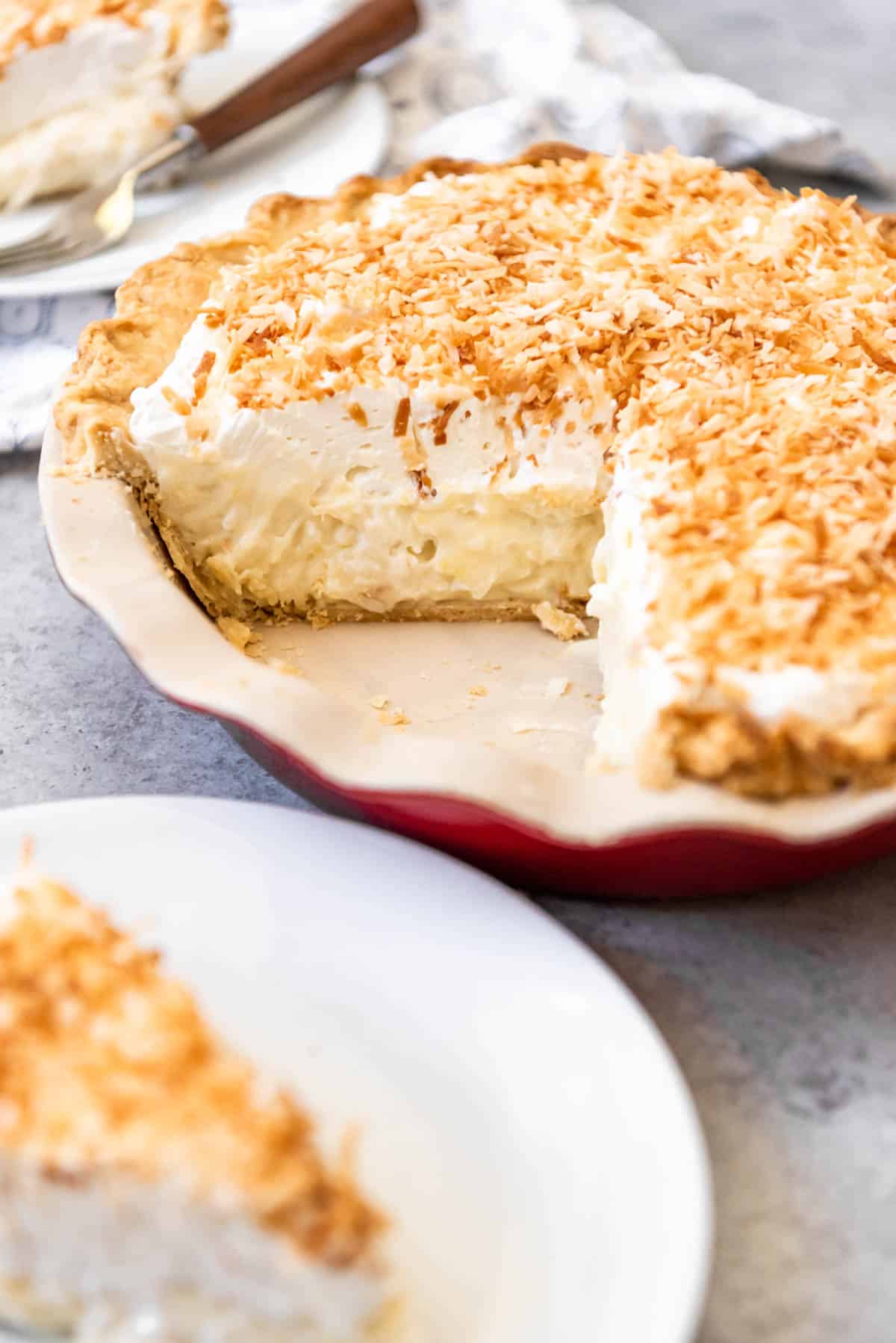 A coconut cream pie with slices removed and placed on plates to the side.