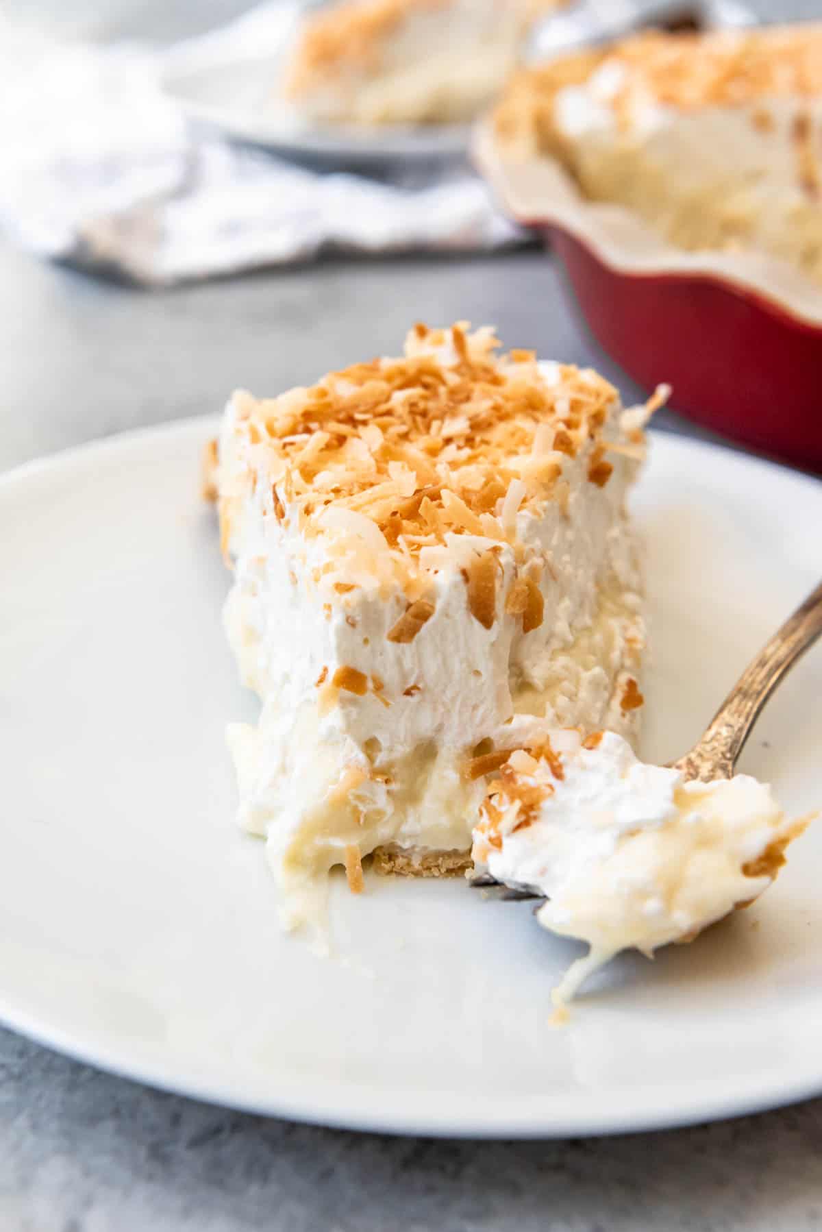 A close image of a slice of coconut cream pie with a bite taken out of it.