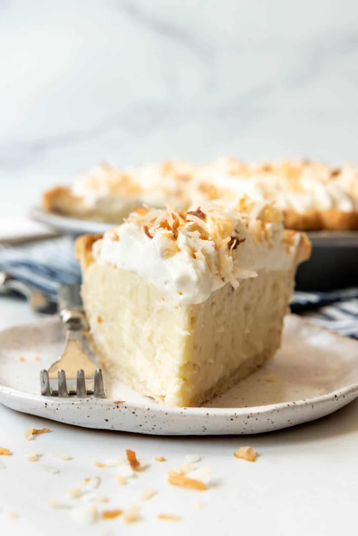 A slice of coconut cream pie on a dessert plate with a fork.