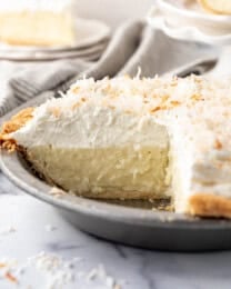 A coconut cream pie with slices removed and placed on plates to the side.