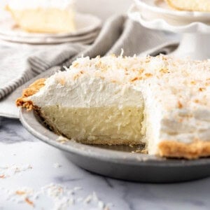 A coconut cream pie with slices removed and placed on plates to the side.