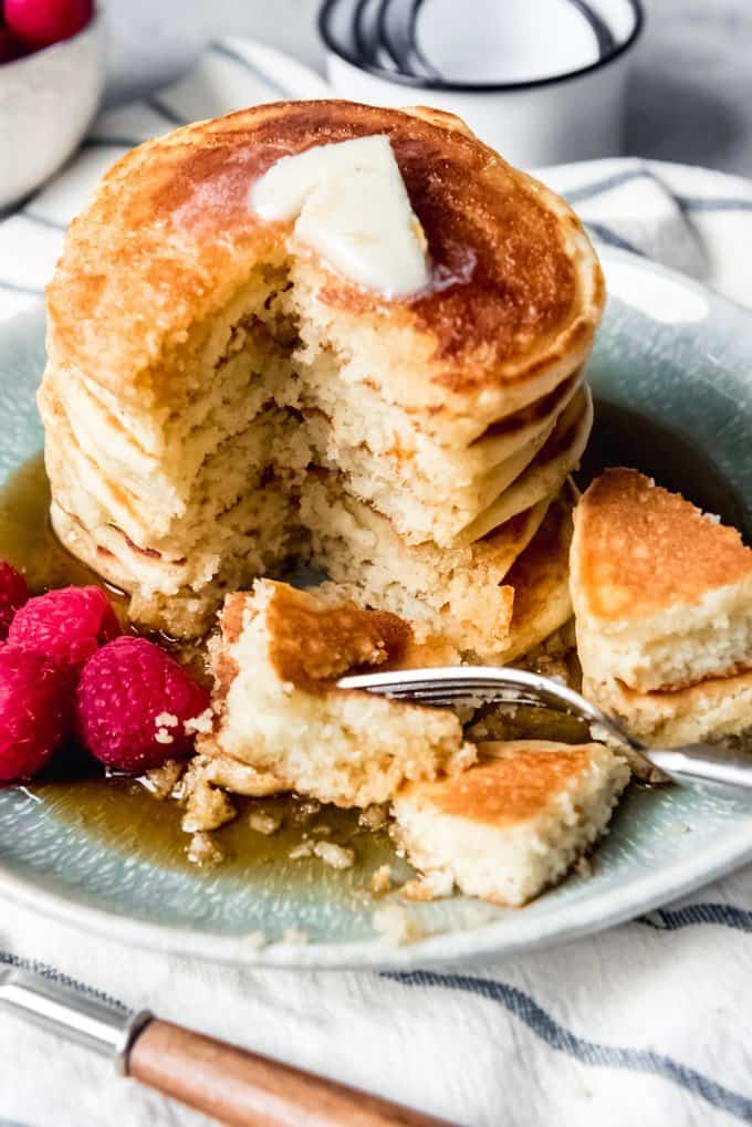 An image of a stack of hoe cakes with butter and syrup and a big bite out of one side.