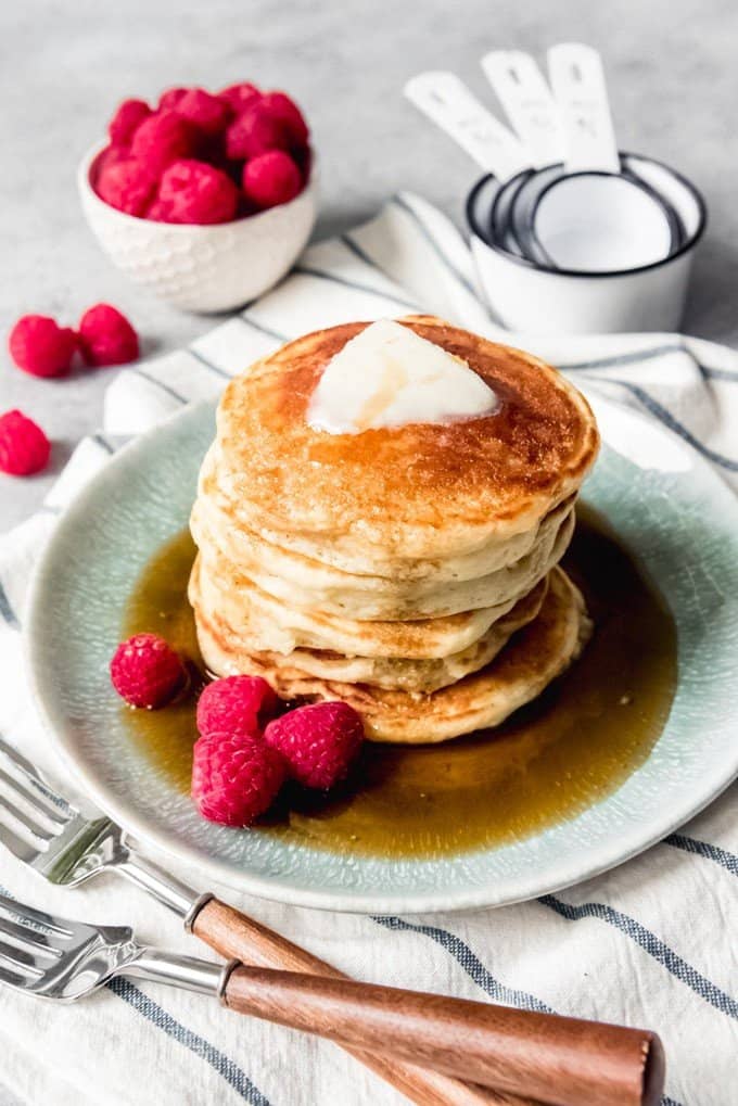 An image of a stack of johnnycakes with butter and maple syrup on top and raspberries on the side.