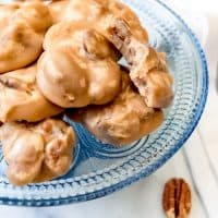 a blue glass plate full of pecan pralines with scattered pecans around it