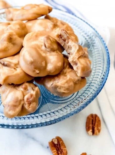 a blue glass plate full of pecan pralines with scattered pecans around it