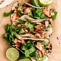 3 salmon tacos arranged side by side with limed halves to the sides