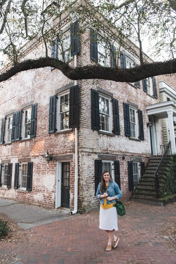 An image of a woman posing on the corner of Jones Street in front of a historic house in Savannah, Georgia.