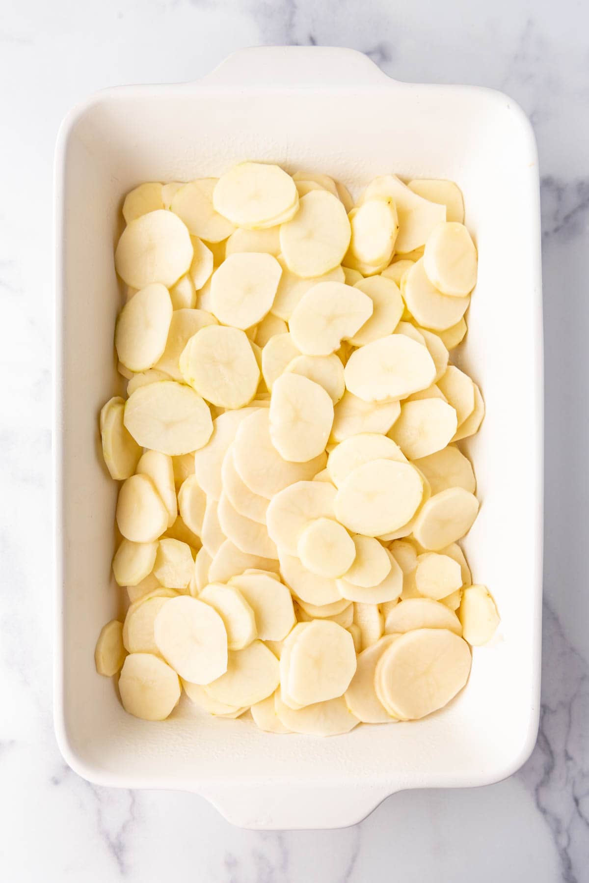 Thinly sliced russet potatoes in a large white baking dish.