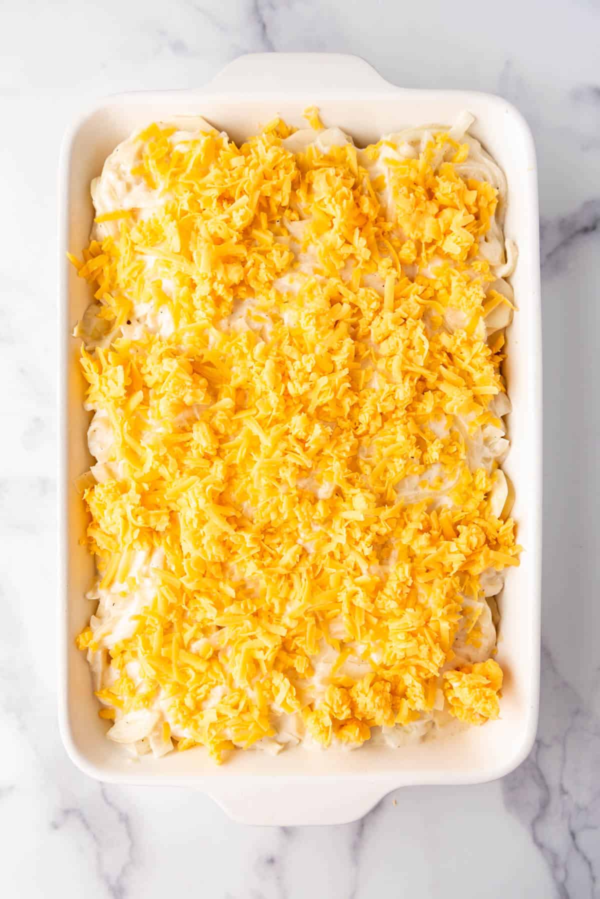 Topping scalloped potatoes with grated cheddar cheese.