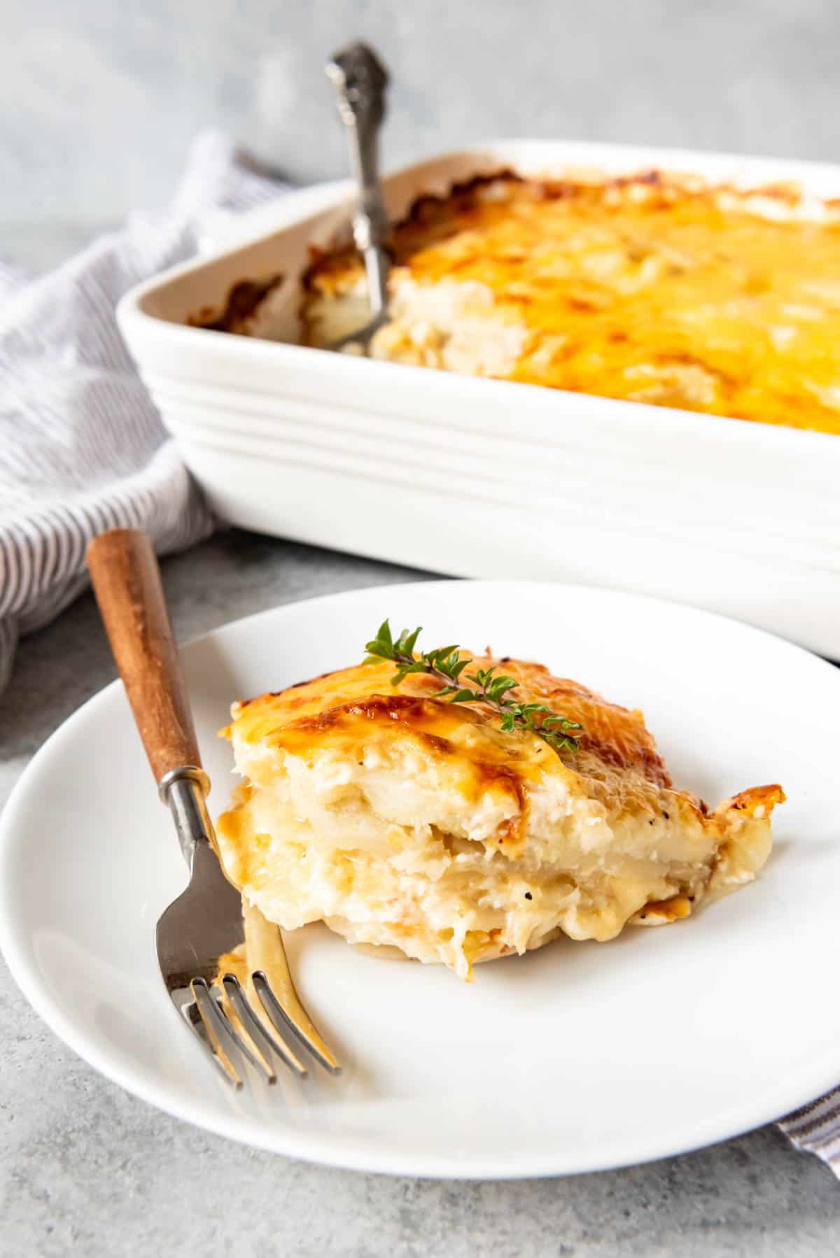 An image of a serving of cheesy au gratin potatoes on a plate next to a casserole dish full of this easy Easter side dish.