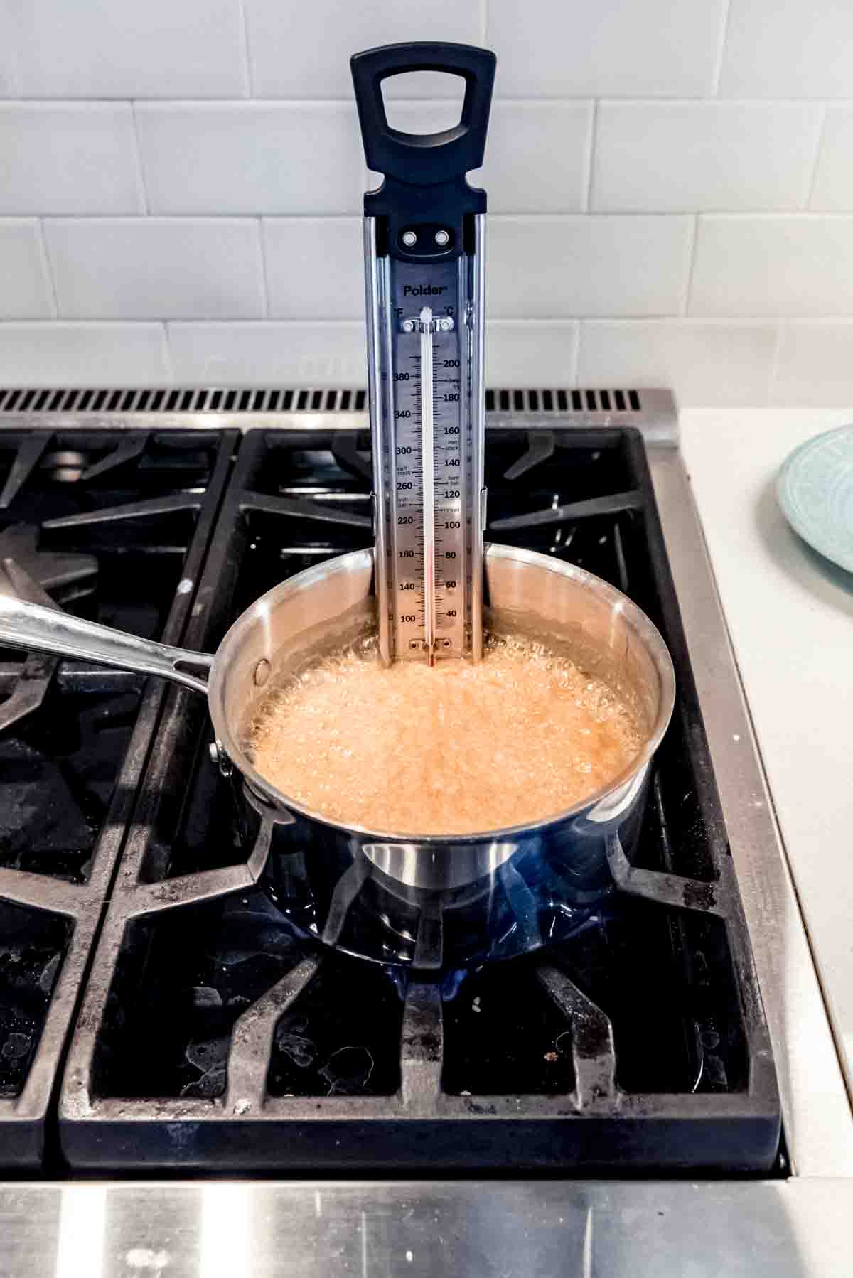 An image of a candy thermometer in a saucepan of boiling sugar.