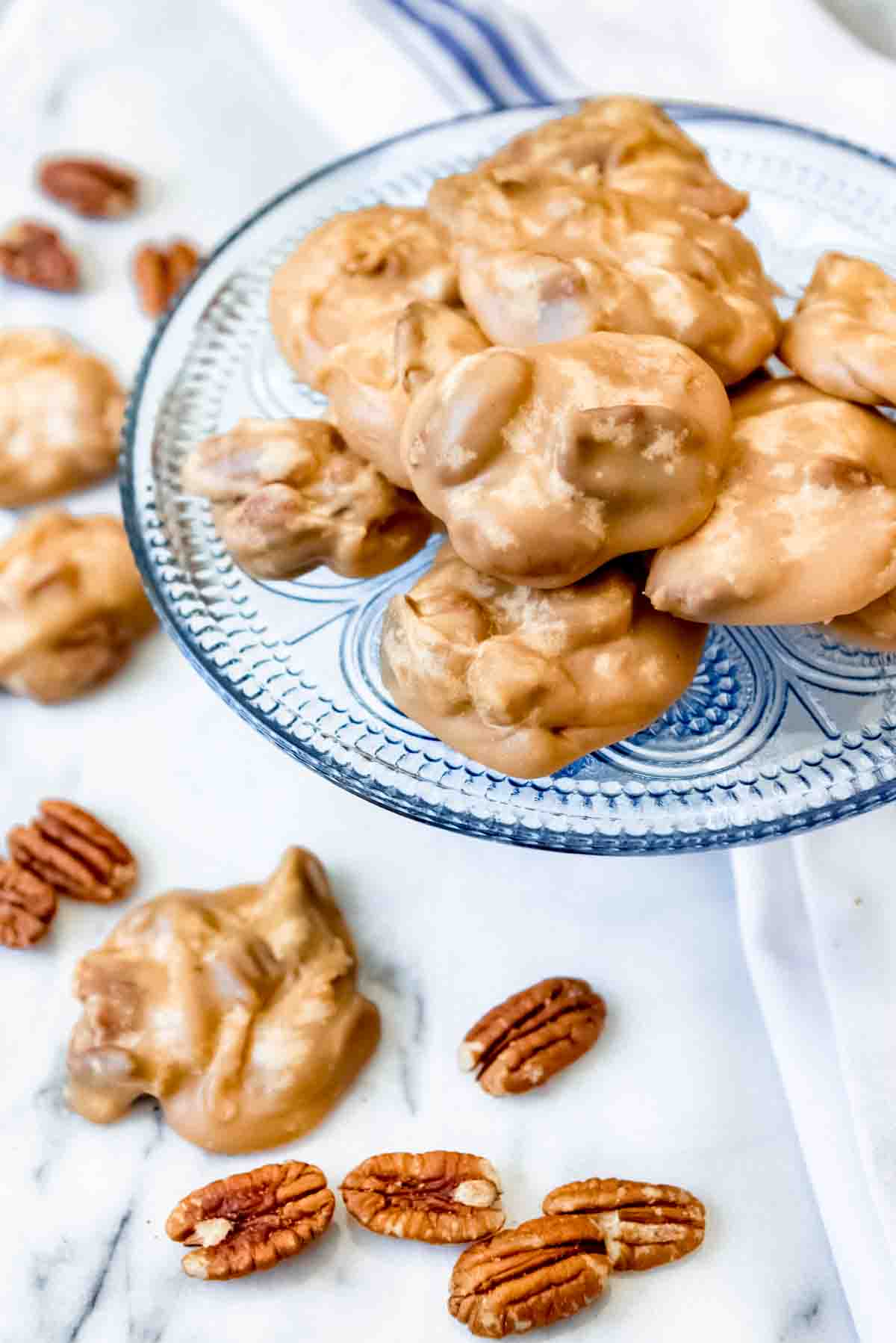 Pecan pralines on and off of a blue plate with scattered pecans around it.