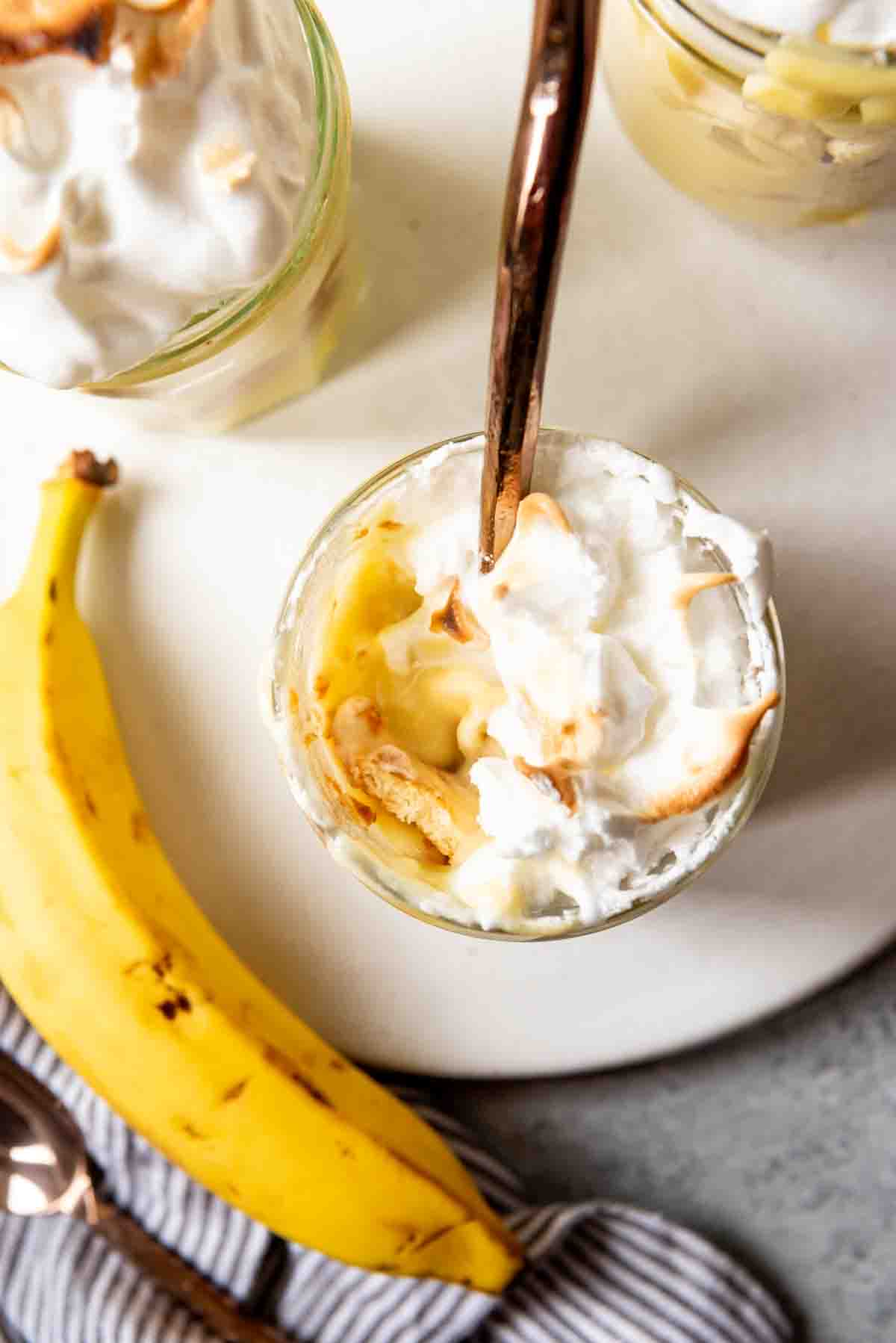 An image of a banana next to a serving of homemade banana pudding with a spoon in it.