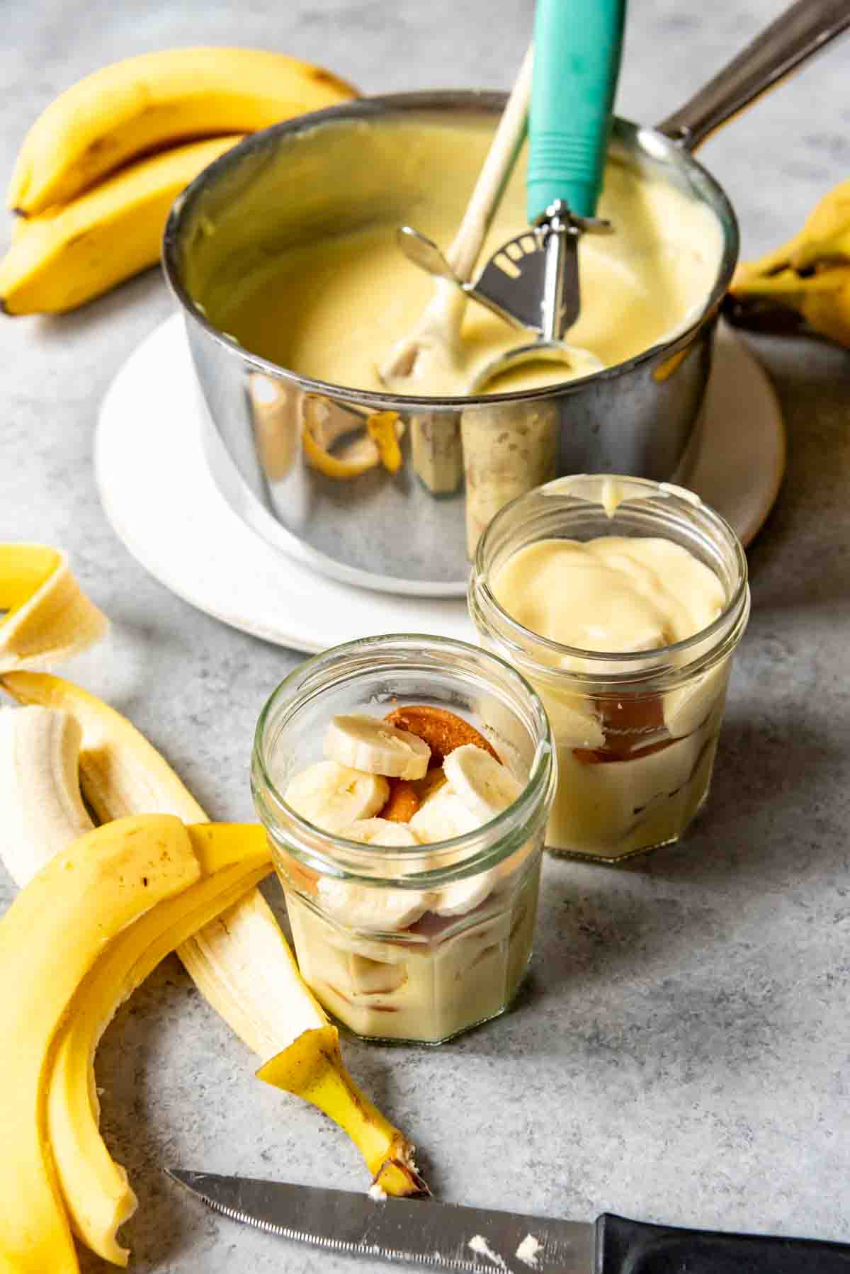 An image of jars filled with homemade pudding, sliced ripe bananas, and Nilla wafers for Southern Banana Pudding.