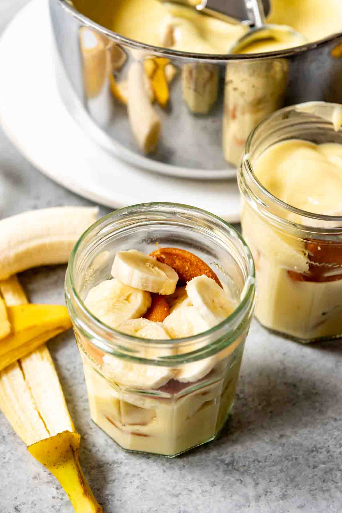 An image of sliced bananas and vanilla wafers in a glass jar with homemade vanilla pudding.