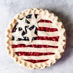 An image of an unbaked cherry and blueberry pie that is decorated with strips of pie dough and stars of cut-out pie dough for a crust.
