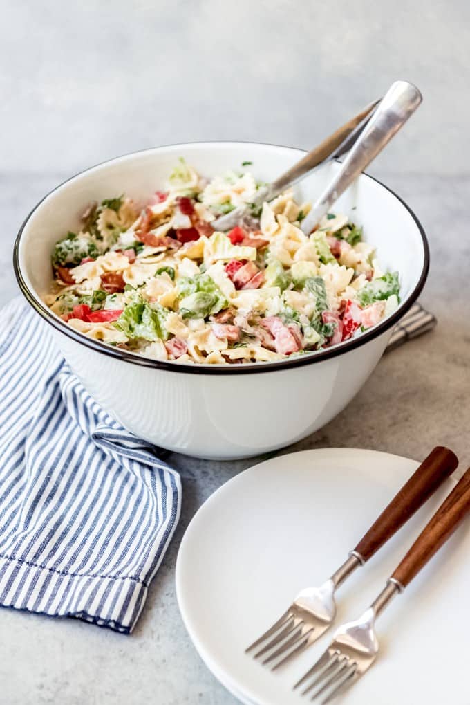 An image of BLT pasta salad in a bowl with serving utensils.