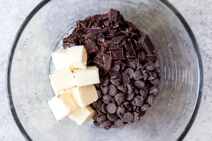An image of butter, chocolate chips, and unsweetened chocolate in a glass bowl.