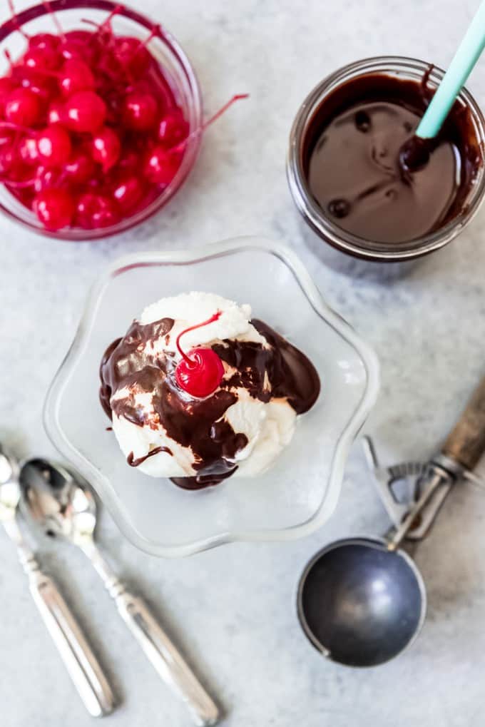 An image of vanilla ice cream covered in microwave hot fudge sauce with a cherry on top.