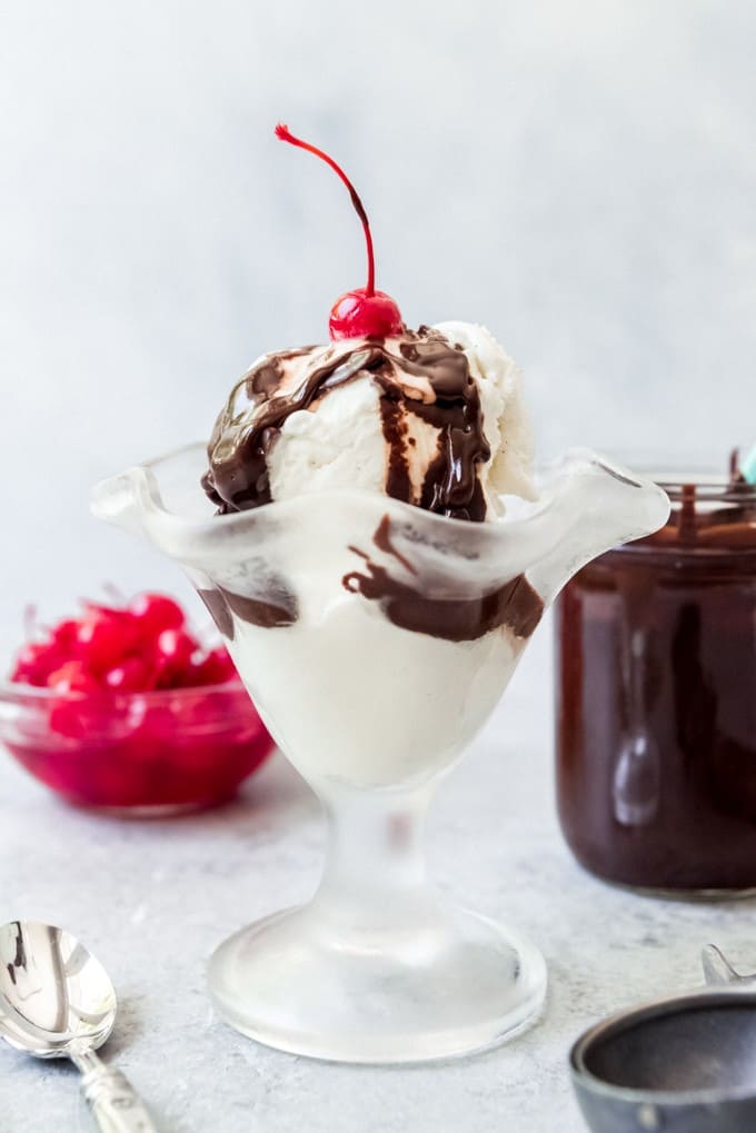An image of an ice cream sundae topped with hot fudge sauce and a maraschino cherry.