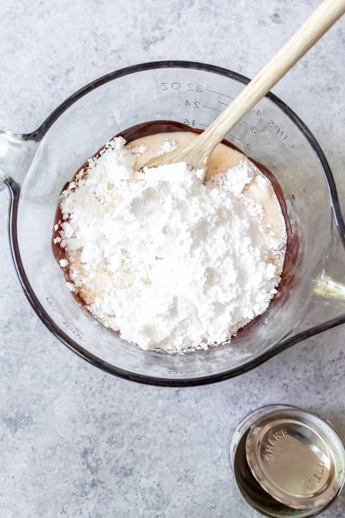 An image of powdered sugar and evaporated milk in a bowl of melted chocolate for making homemade hot fudge in the microwave.