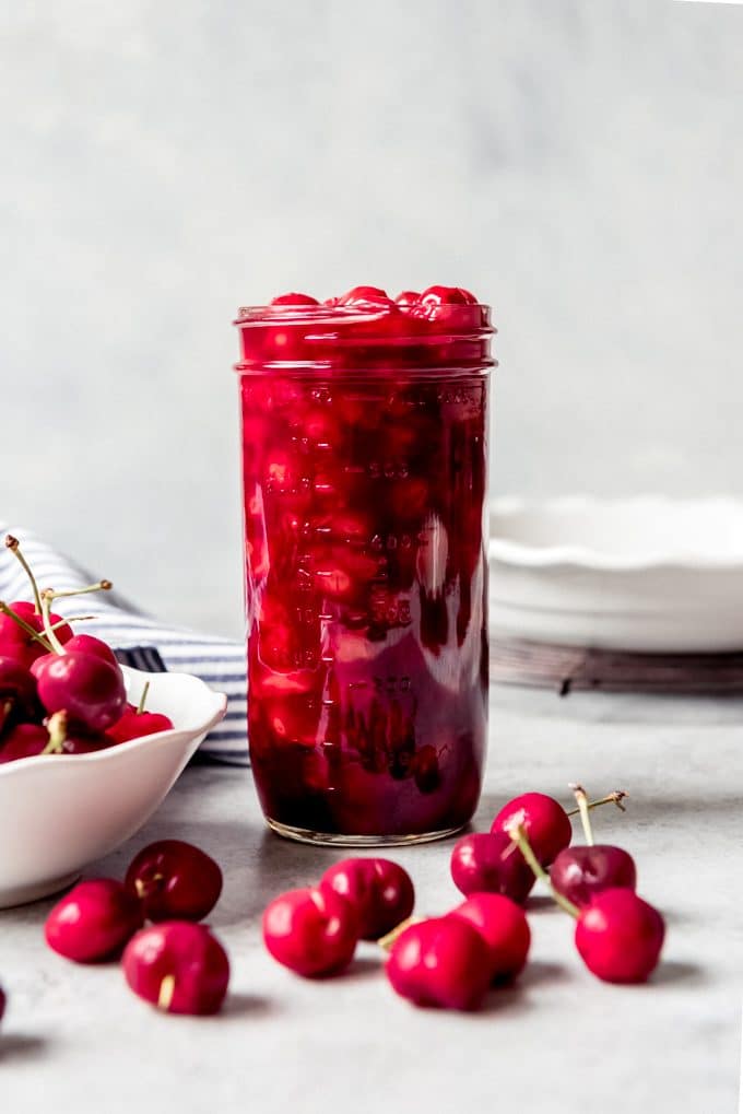 A mason jar filled with cherry pie filling next to fresh cherries.