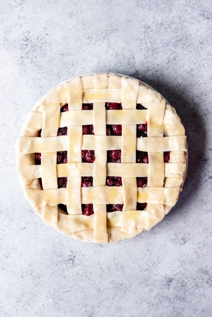 An unbaked cherry pie with lattice crust that has been brushed with egg wash.