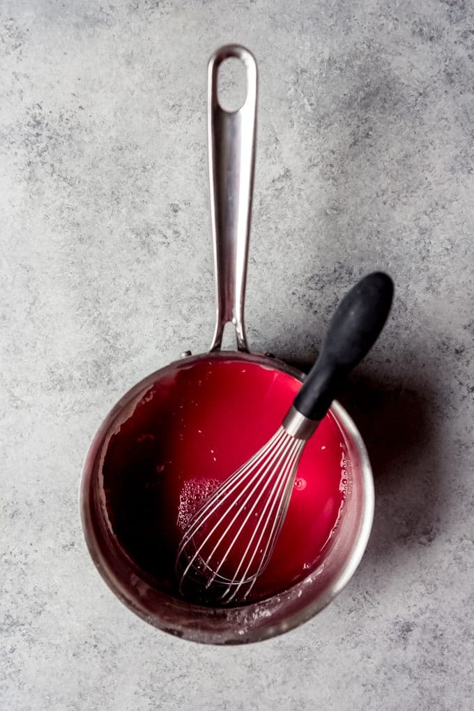 A pot with cherry juice, sugar, cornstarch, and a whisk in it.
