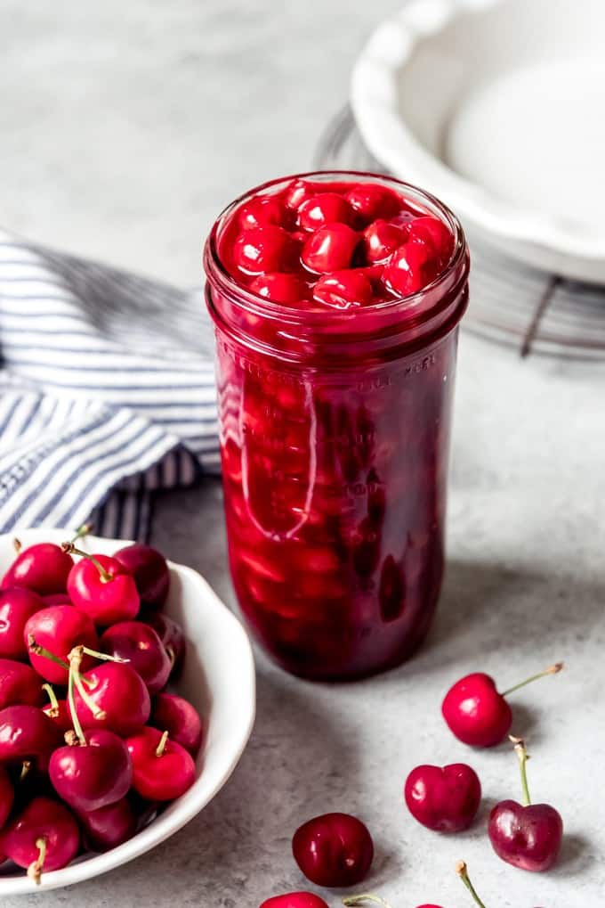 A jar of homemade cherry pie filling next to a bowl of fresh cherries.
