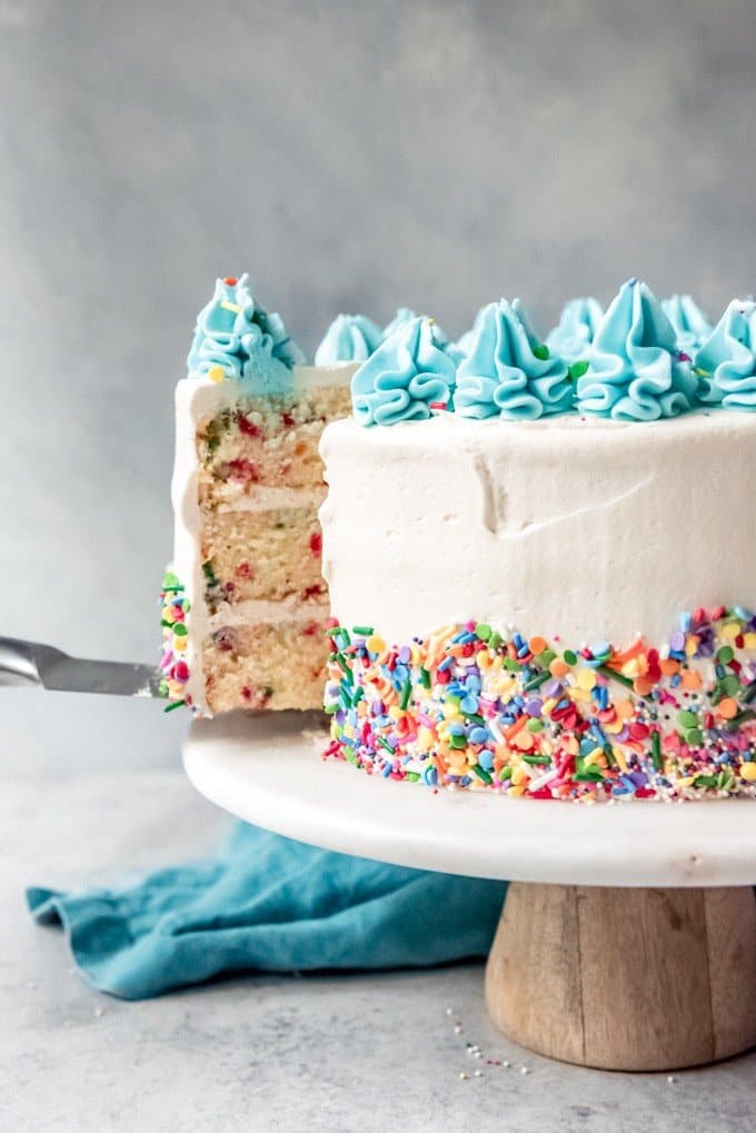 An image of a sprinkle cake with a slice being lifted out of it from the cake stand.