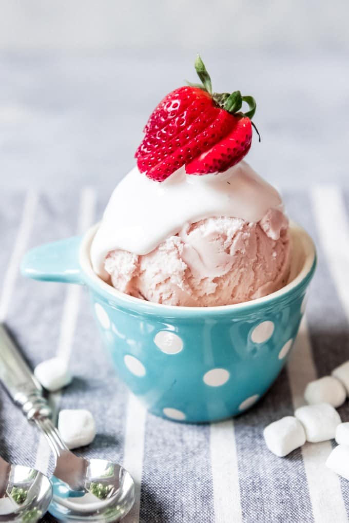 An image of a blue polka dot bowl with strawberry ice cream topped with homemade marshmallow topping and a sliced strawberry.