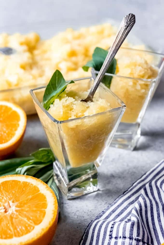 An image of an orange basil coconut granita in a glass with a spoon.