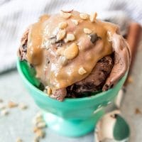 a blue bowl filled with chocolateice cream and topped with peanut butter sauce and chopped nuts