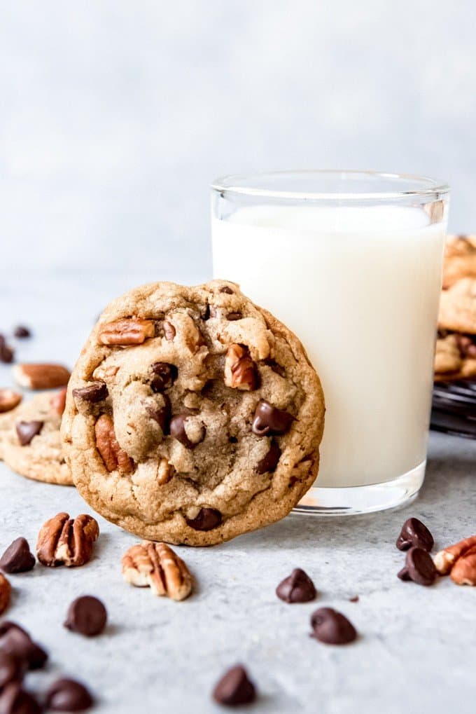 An image of a pecan chocolate chip cookie with a glass of milk.