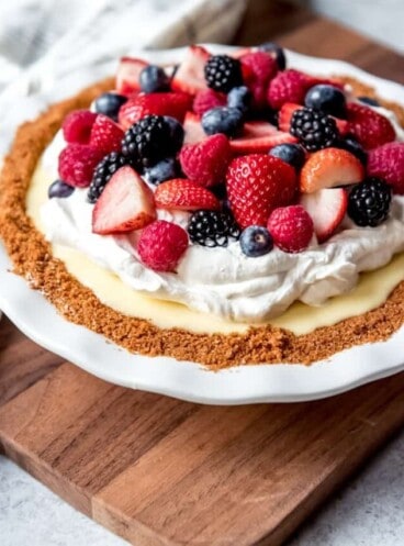 An image of a white chocolate cream pie topped with whipped cream and fresh mixed berries.