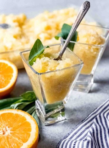 An image of an orange basil coconut granita in a glass with a spoon.