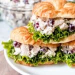 An image of chicken salad sandwiches with grapes stacked on a plate.