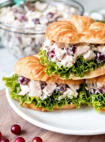 An image of chicken salad sandwiches with grapes stacked on a plate.