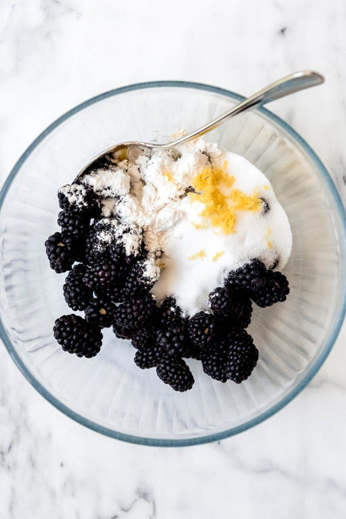 An image of a bowl with blackberries, sugar, flour, and lemon zest for making blackberry filling.