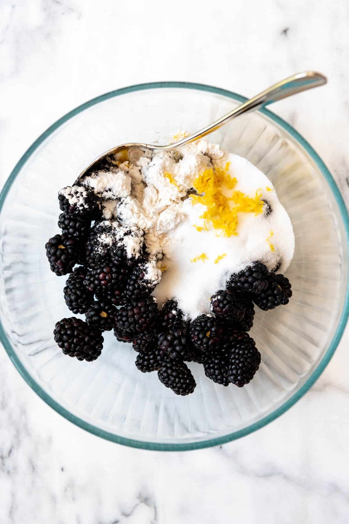 An image of a bowl with blackberries, sugar, flour, and lemon zest for making blackberry filling.