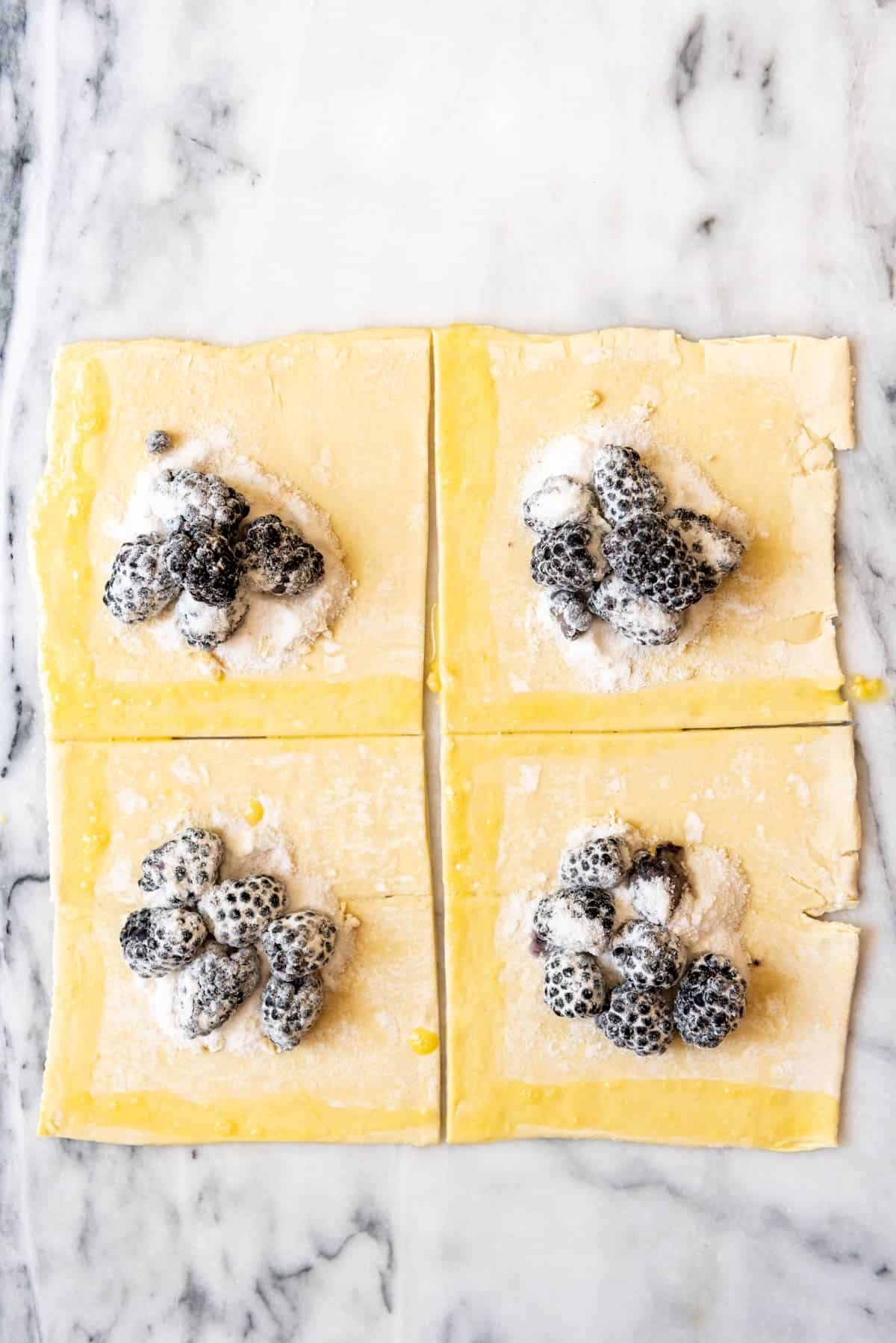 An image of puff pastry squares topped with blackberry filling for making turnovers.