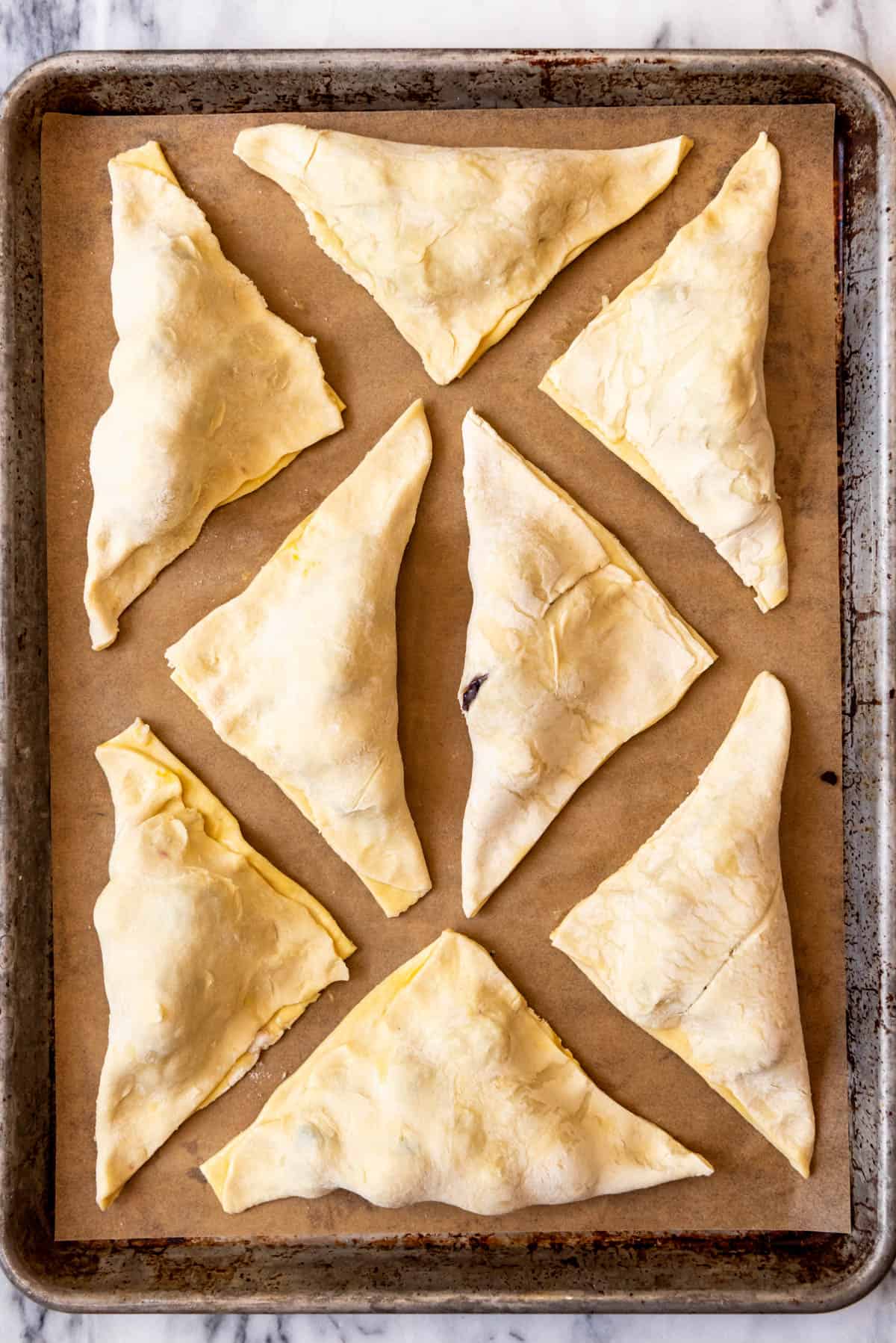 An image of unbaked blackberry turnovers on a parchment-lined baking sheet.