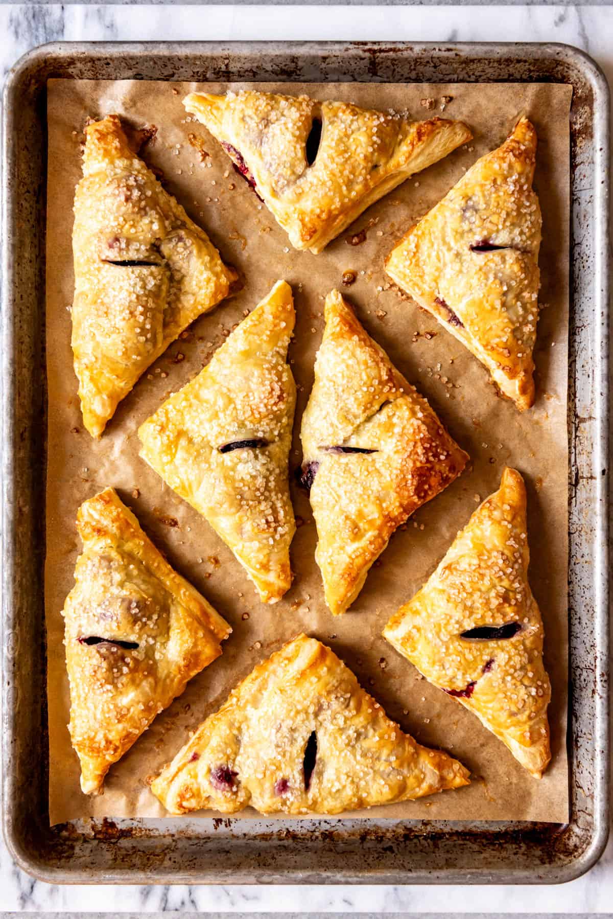 An image of baked blackberry turnovers on a parchment-lined baking sheet.