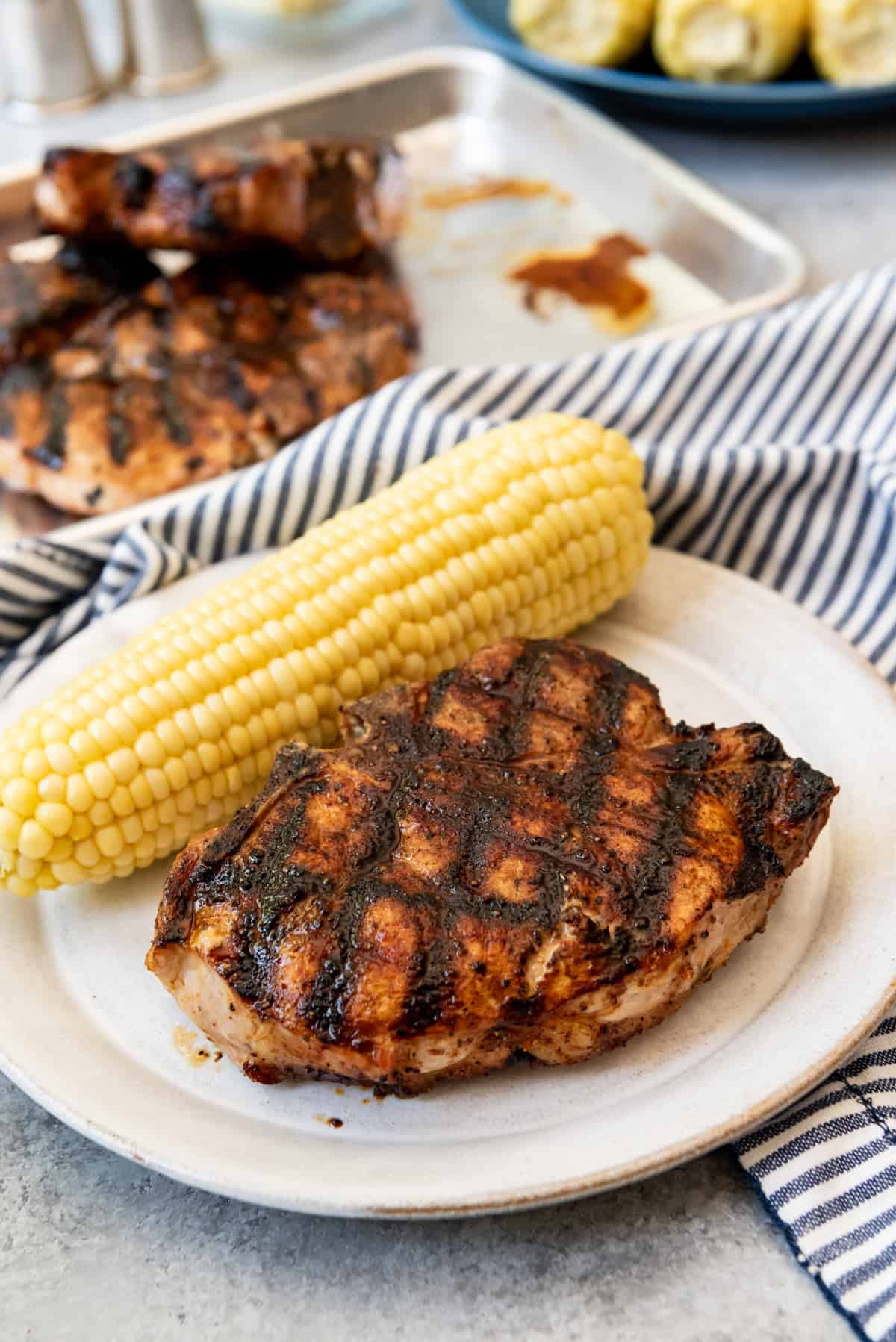 An image of a perfectly juicy grilled pork chop with grill marks on a plate with corn on the cob.