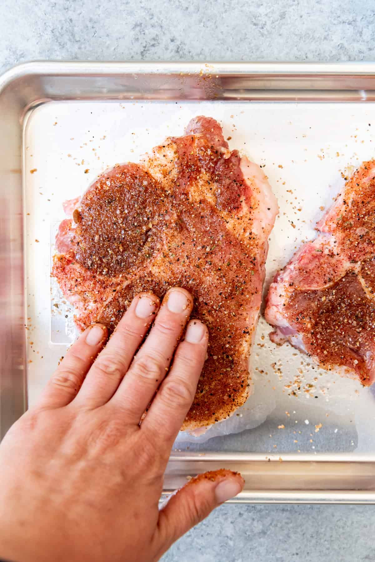 An image of a hand rubbing a bbq spice rub into pork chops for grilling.