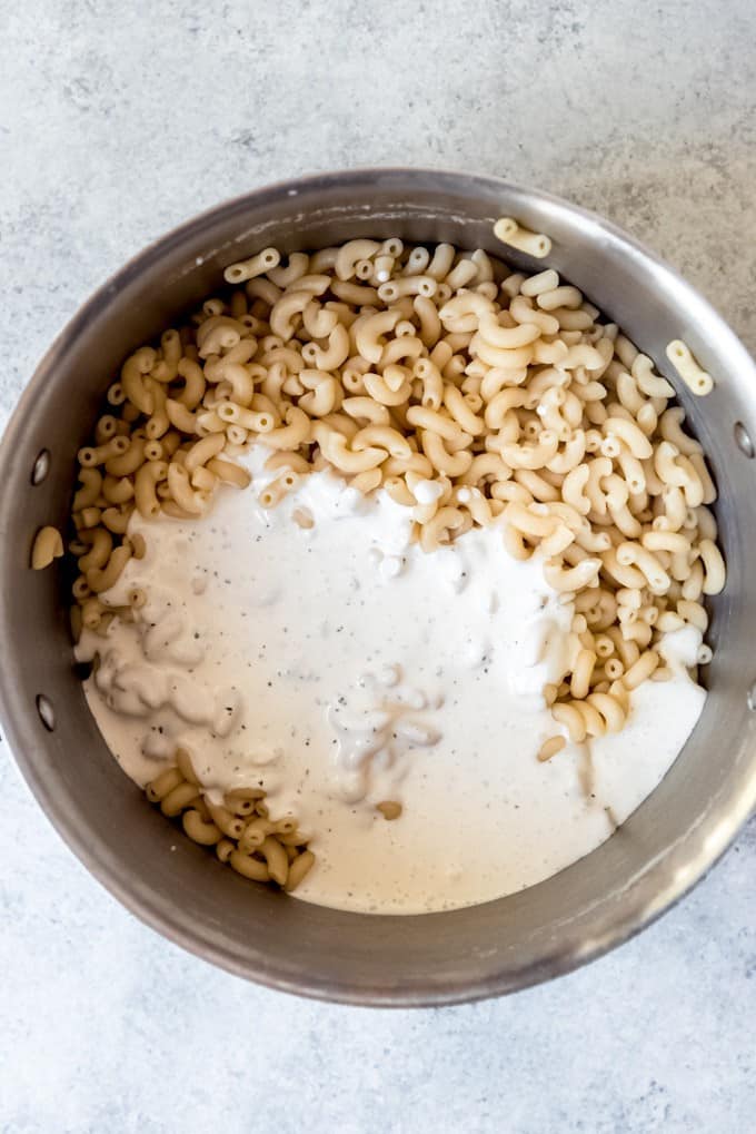 An image of macaroni noodles in a pot with a creamy mayo dressing poured over them for macaroni salad.